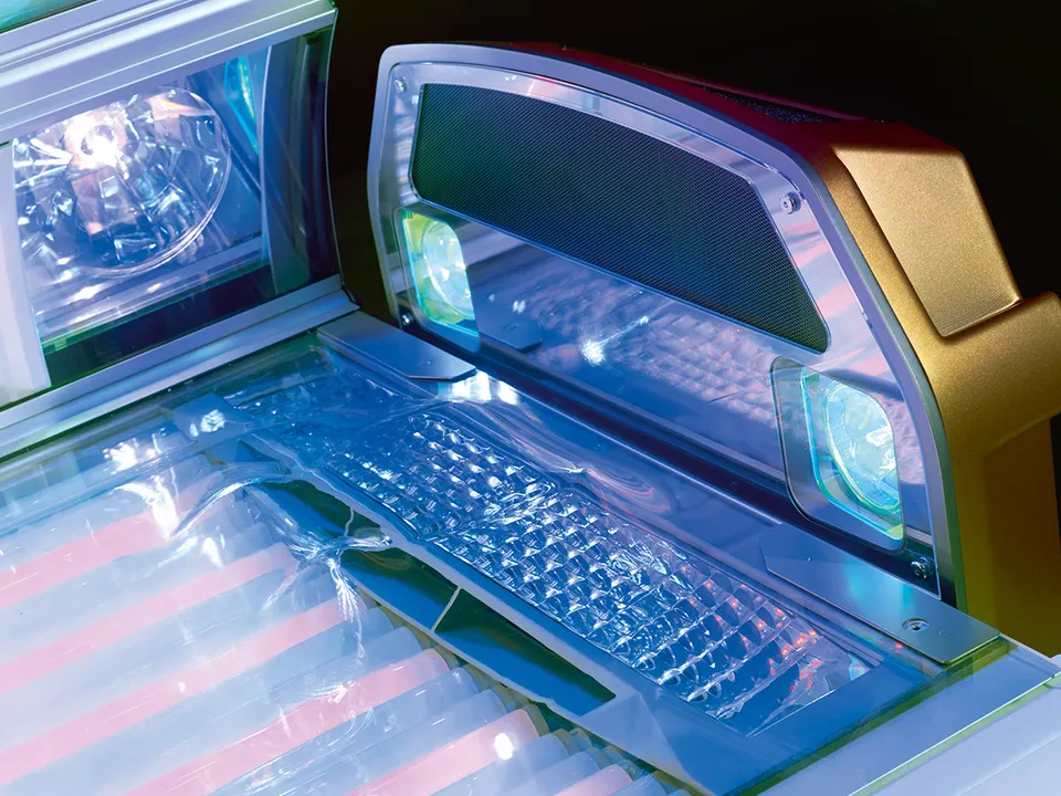 The head end of a Vegaz bench, a lit shoulder tanner either side of a mesh panel, above the ribbed acrylic