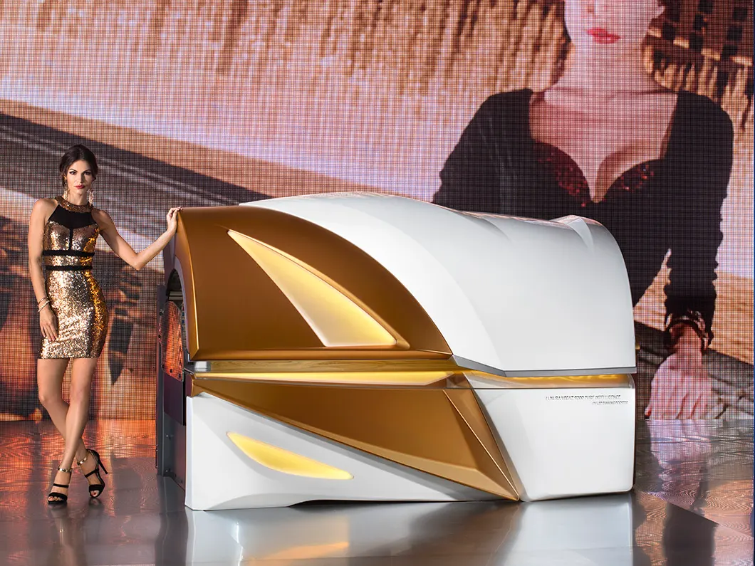 A Luxura Vegaz 9200 in Elite Gold and white, closed and lit, with a model standing beside it